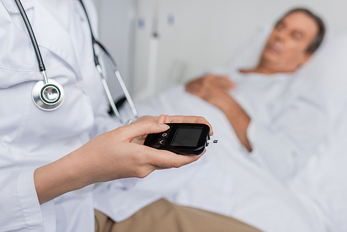 Doctor holding glucometer near blurred patient on hospital bed