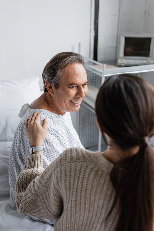 Blurred woman calming smiling senior father in hospital ward