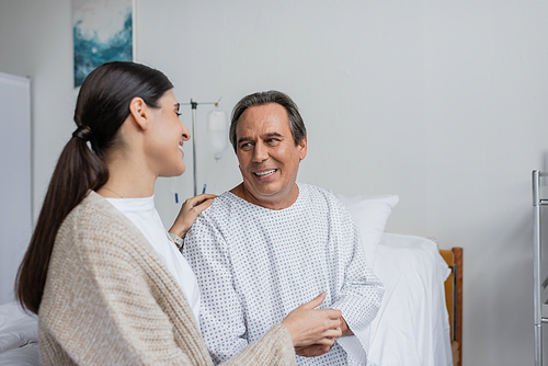 Cheerful patient in gown touching hand of daughter in hospital