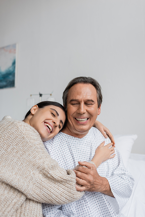 Positive daughter hugging father in patient gown in hospital ward