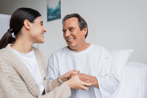 Smiling woman holding hand of father in hospital ward