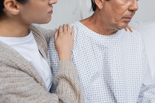 Cropped view of woman hugging senior father in patient gown in hospital ward