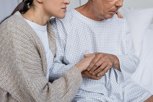 Cropped view of woman calming senior father in patient gown in clinic