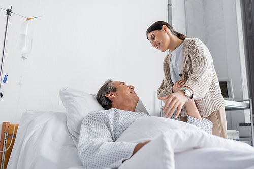 Smiling senior man in patient gown holding hand of daughter in clinic