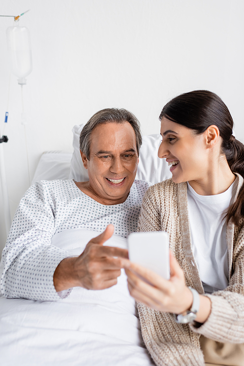 Positive patient pointing at smartphone near daughter in hospital ward