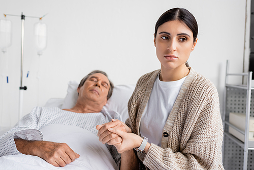 Sad woman holding hand of sick father in hospital ward