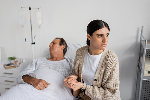 Upset woman holding hand of blurred father in hospital ward