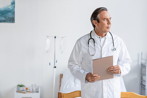 Elderly doctor holding paper folder in hospital ward