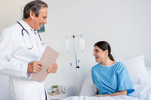 Cheerful patient talking to doctor with paper folder in clinic