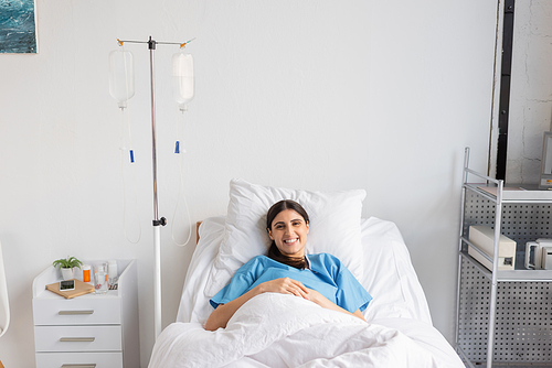 Cheerful patient looking at camera near intravenous therapy in clinic