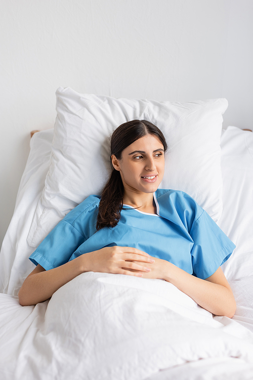 Positive woman in patient gown lying on bed in clinic