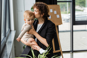 businesswoman in black blazer kissing toddler daughter in office
