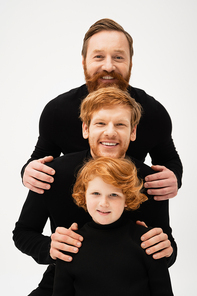happy men in black sweaters smiling at camera near redhead boy while posing isolated on grey