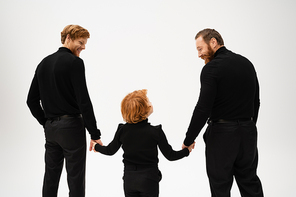 back view of bearded men and red haired boy holding hands and looking at each other isolated on grey