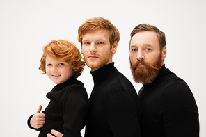 bearded men in black sweaters looking at camera near happy kid showing thumb up isolated on grey