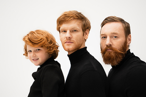 red haired men and smiling boy in black turtlenecks looking at camera isolated on grey