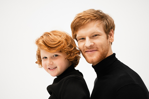 family portrait of redhead dad and son in black sweaters smiling at camera isolated on grey