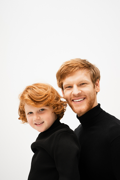 family portrait of red haired father and son in black turtlenecks smiling at camera isolated on grey