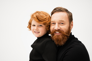 joyful bearded man with redhead grandson smiling at camera isolated on grey