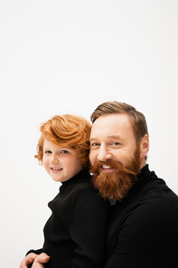 happy bearded man and redhead grandson wearing black sweaters and looking at camera isolated on grey