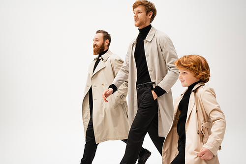 smiling red haired men and boy in stylish trench coats walking isolated on grey