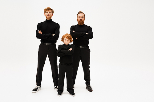full length of redhead men and boy in black clothes posing with crossed arms on light grey background