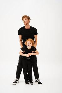 full length of redhead man lifting cheerful son while having fun on light grey background