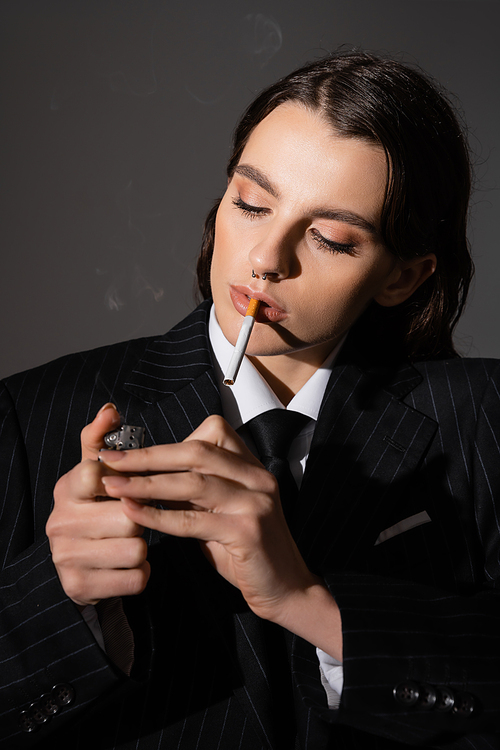 portrait of young model in formal wear lighting cigarette isolated on dark grey