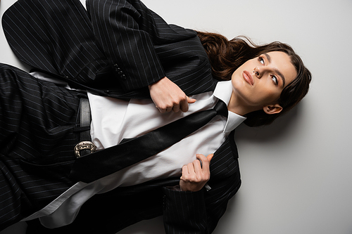 top view of young woman looking away while lying in stylish formal wear on grey background