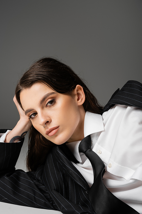 portrait of pretty model in white shirt with black blazer and tie looking at camera while lying on grey