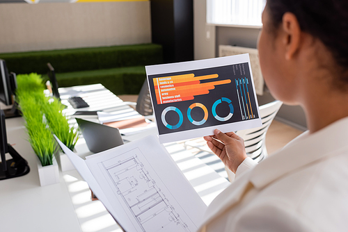 blurred multiracial businesswoman holding charts and blueprint while working in office