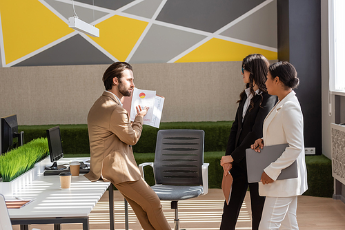 side view of businessman showing graphs to multicultural colleagues in modern office