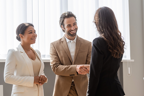 happy man shaking hands with business partner near smiling multiracial colleague