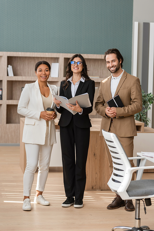 full length of happy multiethnic business people in formal wear looking at camera while standing in office