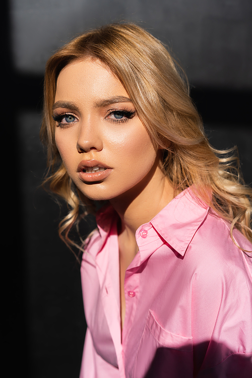 portrait of young woman in pink shirt looking at camera on black background
