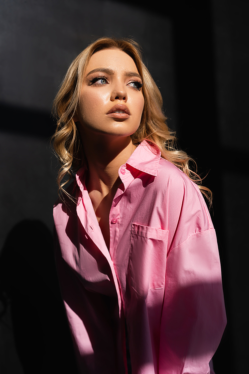 young woman in pink shirt looking away while posing in lighting on black background