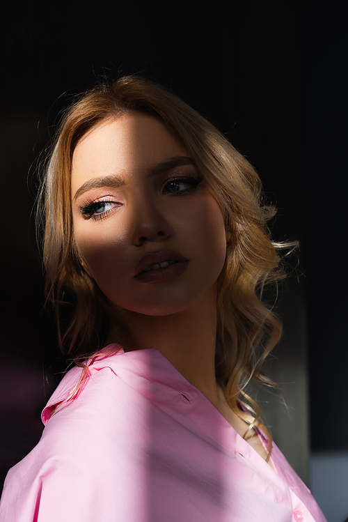 portrait of charming woman with wavy hair looking away in lighting on dark background