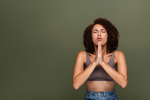 Curly african american woman with closed eyes praying isolated on green