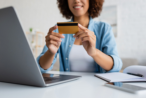 Cropped view of blurred african american woman holding credit card near devices