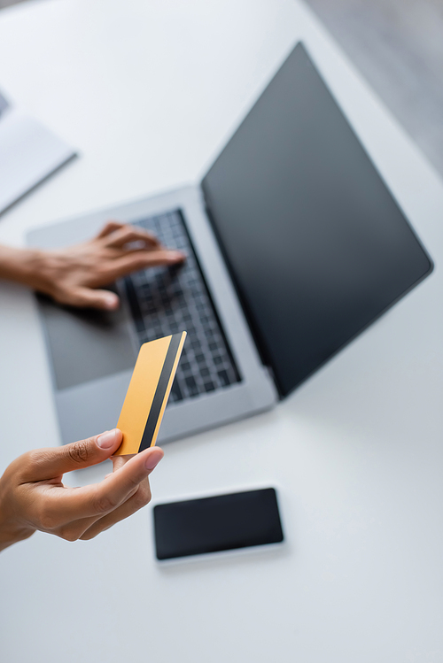 Cropped view of african american woman holding credit card and using laptop with blank screen at home