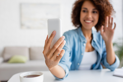 Blurred african american woman having video call on smartphone near cup of tea at home