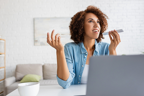 African american woman recording voice message on smartphone near laptop and tea