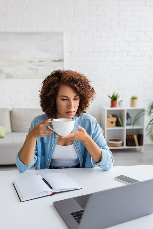 African american freelancer holding cup near gadgets and notebook on table