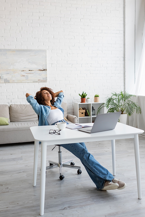 pleased african american woman with closed eyes resting near workplace at home