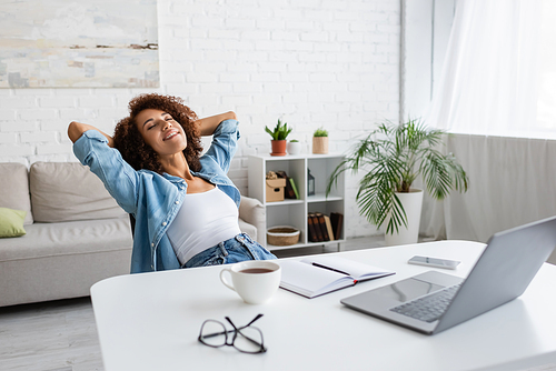 cheerful african american woman with closed eyes resting near workplace at home