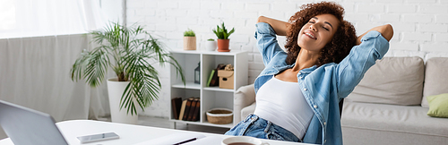 cheerful african american woman with closed eyes resting near workplace at home, banner