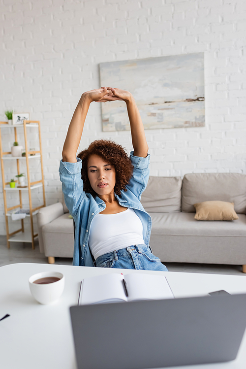 tired african american woman with curly hair stretching near workplace at home