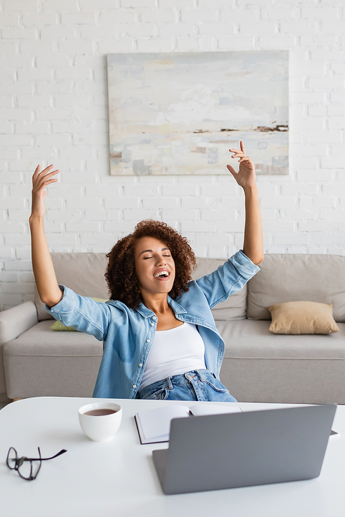 cheerful african american woman with closed eyes rejoicing near workplace at home