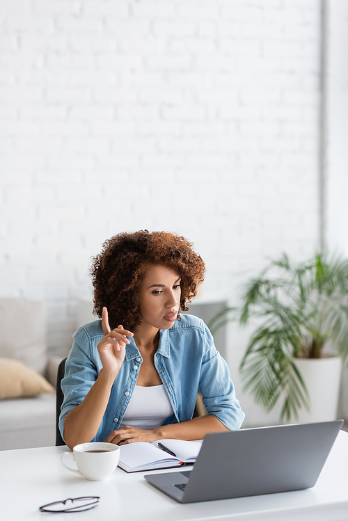 curly african american freelancer pointing with finger during video call on laptop