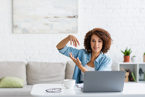 curly african american woman gesturing during video call on laptop